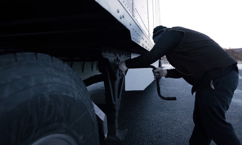 Fahrer bedient manuell die Stützfüße eines Lastwagenanhängers auf Asphalt