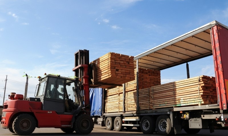 Gabelstapler lädt Holzpaletten auf einen Sattelzug unter blauem Himmel